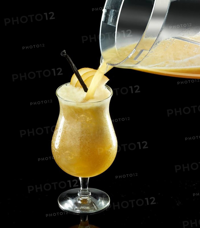 Orange-colored cocktail is poured onto ice cube cubes, against a black background, apple slices and vanilla bean as a garnish, studio shot