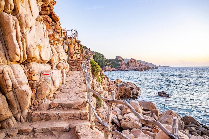 A little trail passing the rocks at the coastline with blue water at Costa Paradiso on a sunny day at sunset, Sardinia, Italy