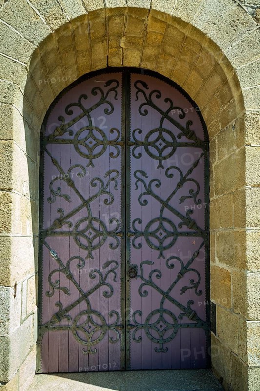 Ornate purple door set in a stone archway. porch of romanesque church of Saint-Saturnin. Puy de Dôme. Auvergne. France