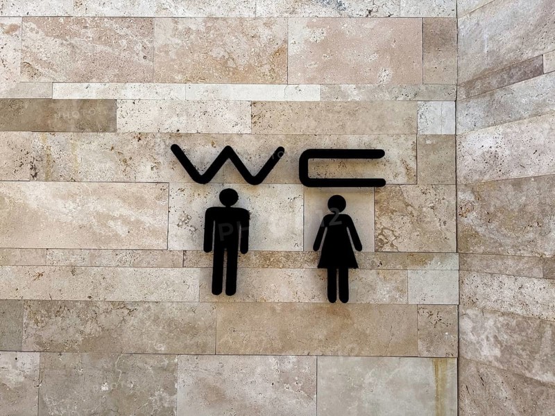 Restroom sign with male and female symbols on a textured stone wall. Clear indication of facilities for men and women