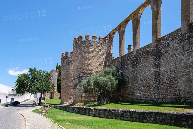 Massive medieval walls with arches next to a road and green meadow, Serpa, Beja, Portugal