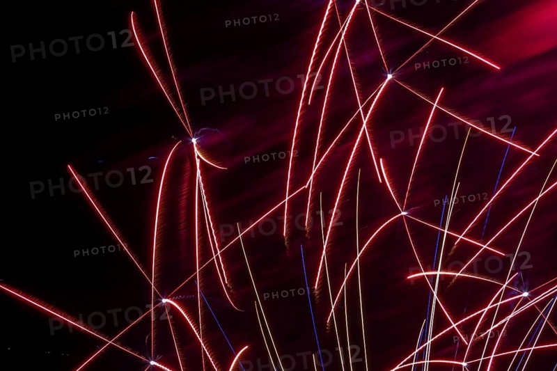 Red, white and blue illuminated trailing streaks of fireworks in black sky at night in summer, Quebec, Canada