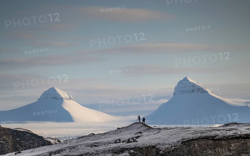 Two people, including a photographer with a stand in front of two of the three mountains Tee Kroner, Kongsfjord or Kongsfjorden, Spitsbergen archipelago, Svalbard, Norway