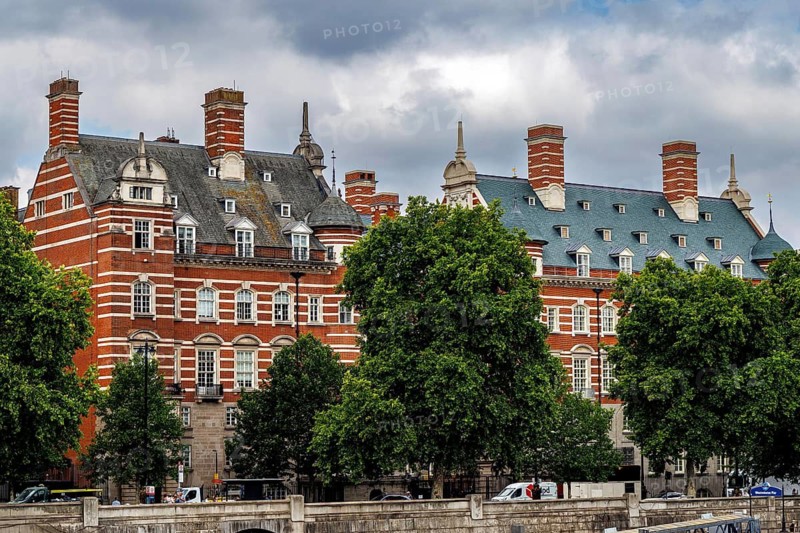 Mature riverside trees frame the ornate red brick facade of the Norman Shaw Building on Victoria Embankment, designed by Richard Norman Shaw and built between 1887 and 1906 as the original New Scotland Yard. It served as Metropolitan Police headquarters until 1967, London, England, United Kingdom