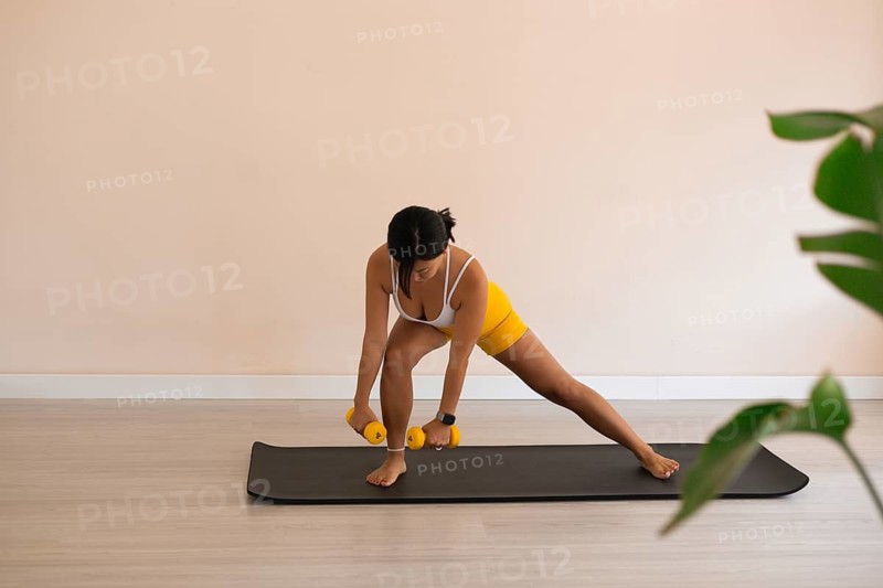 A woman in a side lunge position with dumbbells, focusing on strength training on a yoga mat