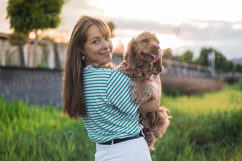 A joyful woman smiling at the camera while holding her dog during sunset in a park