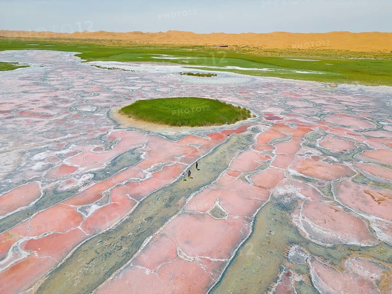 Aerial view of Camel Lake set against shifting sand dunes, caused by microorganisms and algae such as Dunaliella salina, which produce the pigment beta-carotene to protect themselves from strong UV radiation, A salt lake near the well-known Ulan Lake in the Tengger Desert, part of the Gobi Desert known as the ‘red heart of the Earth', Inner Mongolia, China