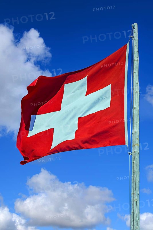 Swiss flag waving against blue sky, cumulus clouds, Swiss national flag