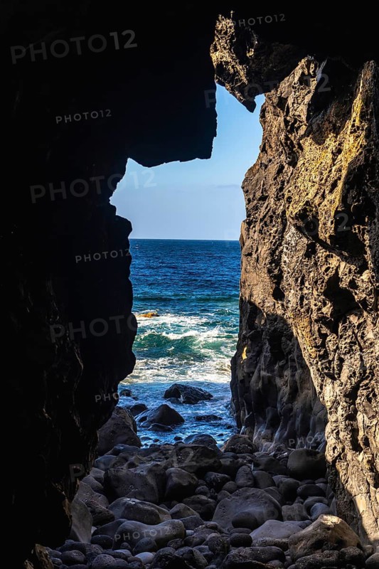 Dark lava rock cave revealing the dramatic blue atlantic ocean with white waves crashing upon the rocky shore, highlighting the rugged volcanic landscape of the canary islands