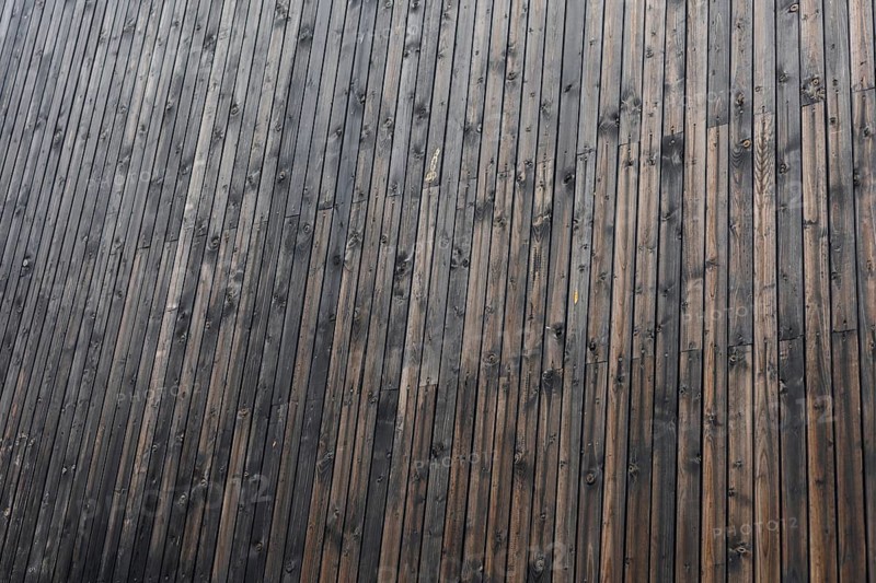 Close-up of a textured wooden surface with dark brown and black tones. The wood has a natural grain pattern and slight imperfections