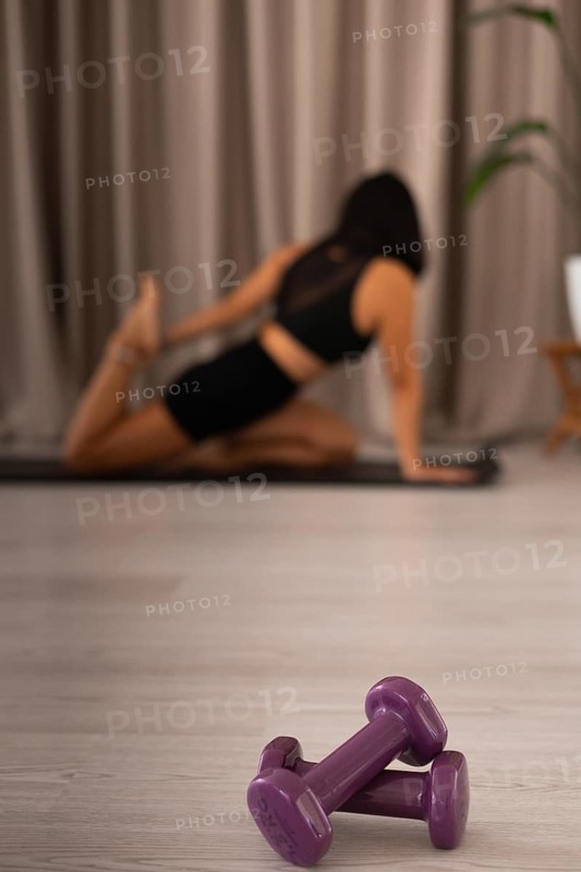 Purple dumbbells in focus with a stretching woman in a blurred background