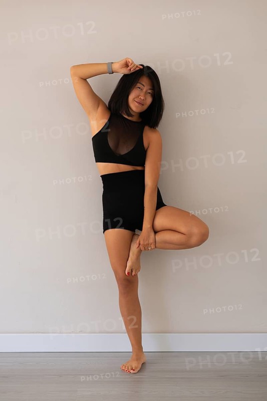 Woman standing in a tree yoga pose against a neutral wall in a studio
