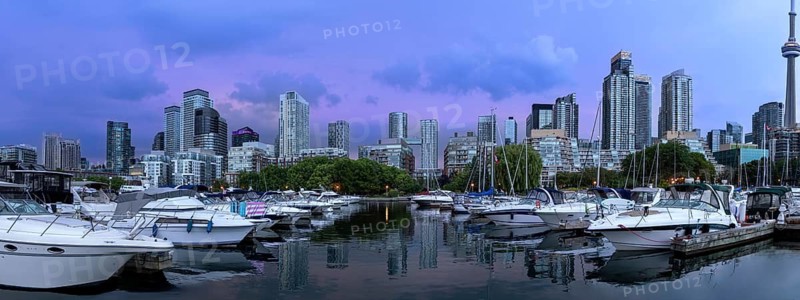 Yachts and sailboats moored at a harbour marina with high rise skyline buildings and skyscrapers under a sunset sky near downtown and Toronto Islands