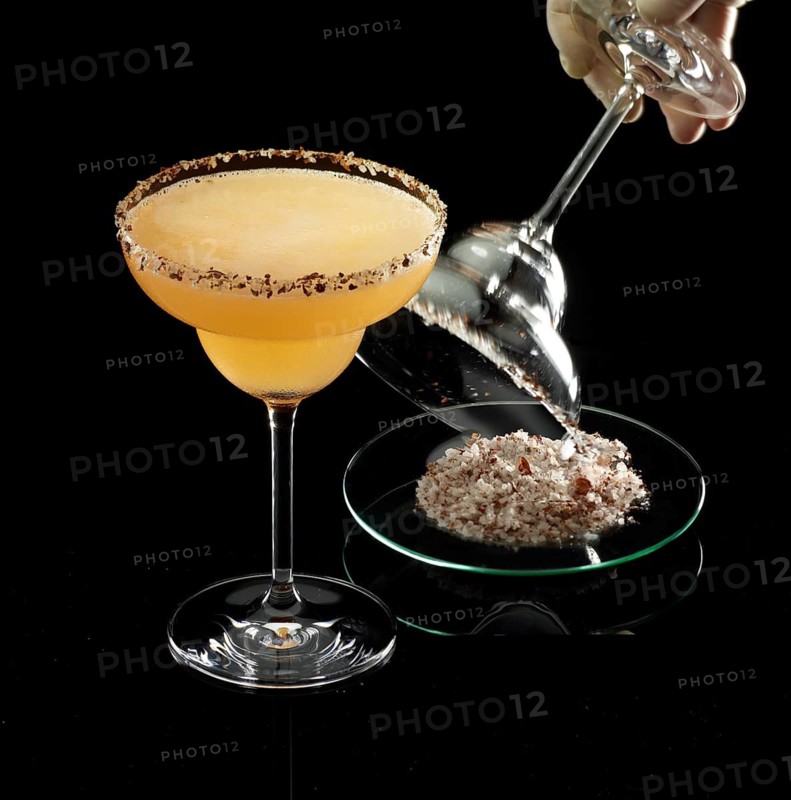 Orange-colored cocktail on a black background, salt rim as a garnish, glass with salt rim is prepared next to it, studio recording