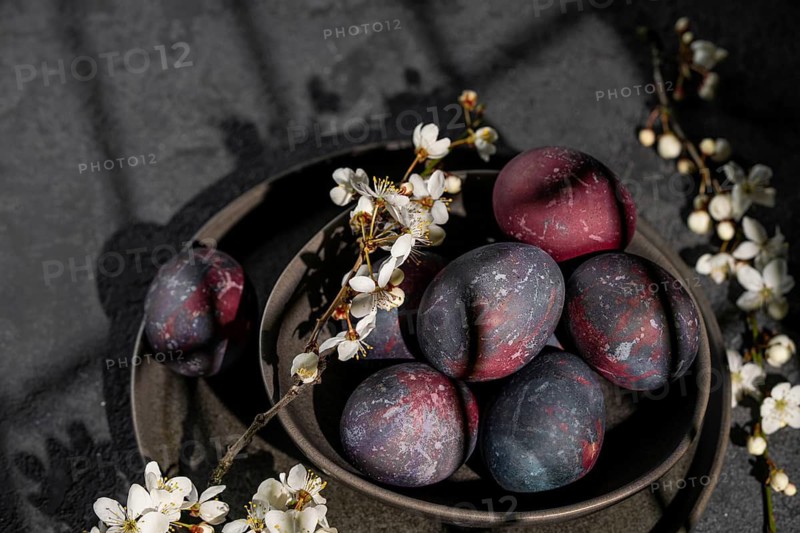 From above, a rustic bowl filled with galaxy-inspired Easter eggs sits amid delicate white flowers and branches, showcasing a creative and atmospheric representation of Easter celebrations