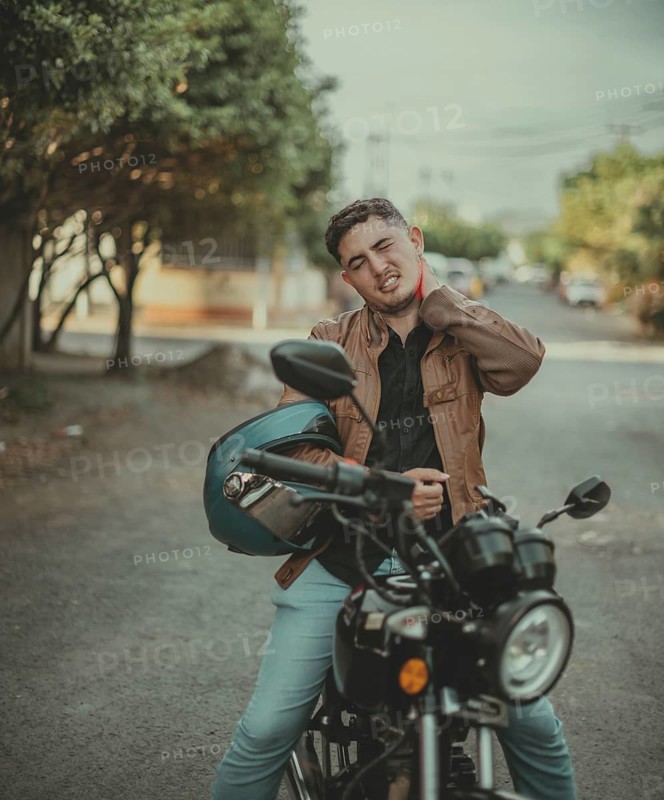Young motorcyclist suffering from neck pain on the road. Male motorcyclist with stress and neck pain on the street