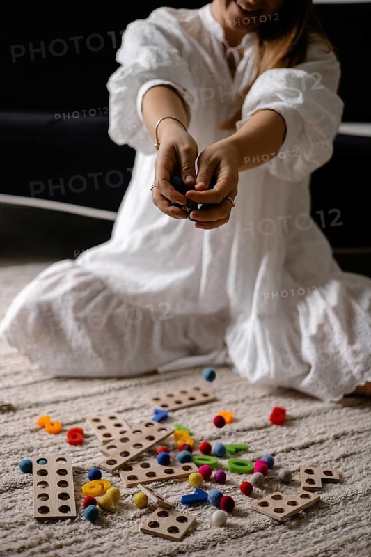 Person in white dress kneeling with scattered wooden toys and colorful balls
