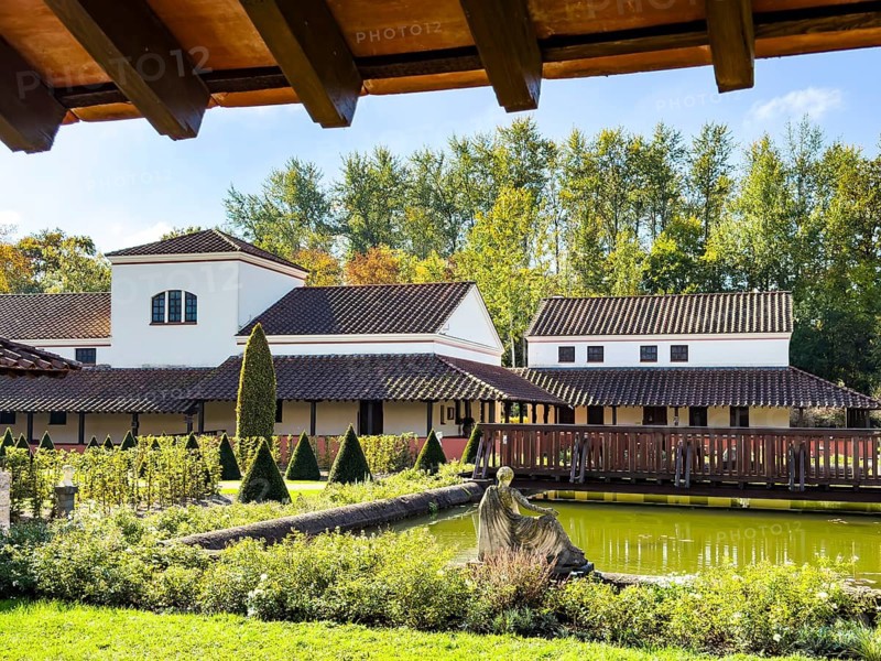 View from site of archaeological open-air museum across small wooden bridge across ornamental pond to reconstructed side wing with restaurant in open-air museum Archaeological Park Römische Villa Borg, Perl, Saarland, Germany