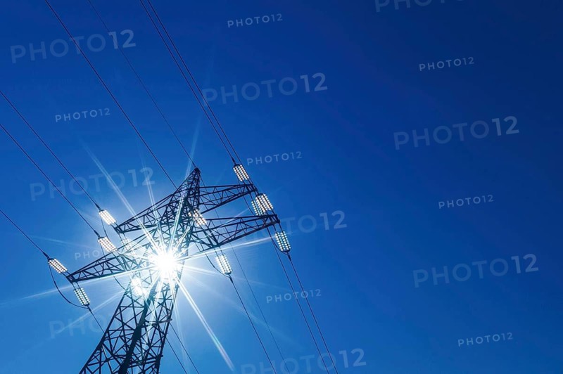 The sun shines through a tower of a high-voltage line for electricity. Sonnenenergie, Austria