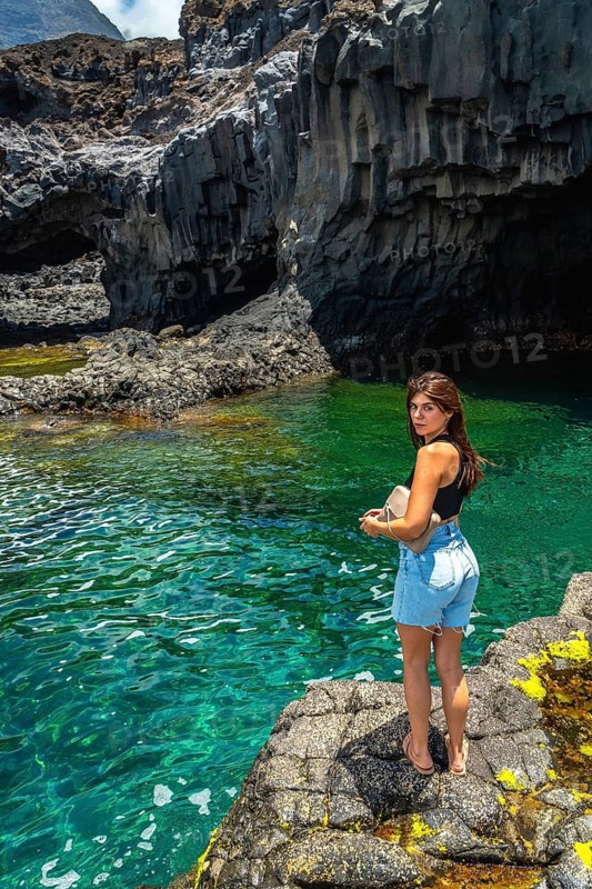 Young woman standing on volcanic rocks by clear turquoise water, enjoying a sunny summer day exploring the natural beauty of el hierro island in the canary islands