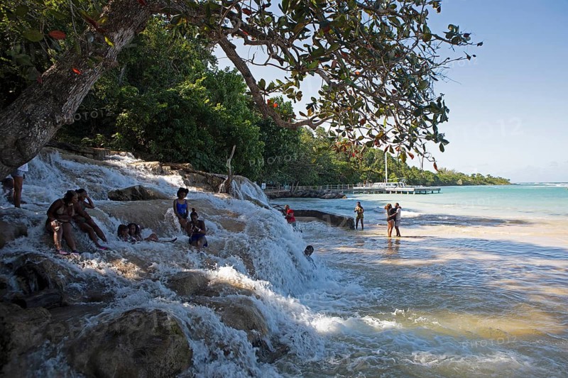 Jamaican woman sit on rocks at Dunn's River Falls or waterfalls at the mouth of the Caribbean Sea, Ochos Rios, Saint Ann Parish, West Indies, Caribbean, Central America