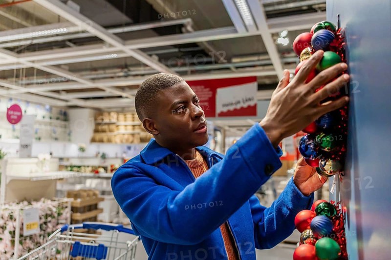 A close-up on a man's hand placing a garland on a blue wall. Christmas wreath has red, green balls