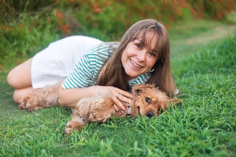 Woman joyfully posing in the grass with her dog, exuding friendliness and joy