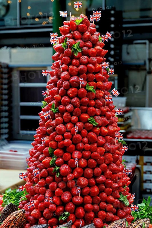 Glossy strawberries are stacked into a tall pyramid and trimmed with mint leaves and miniature Union Jack flags outside a fruit stall in Southwark, a colourful seasonal display reflecting Borough Market's long reputation as one of London's leading food destinations, London, England, United Kingdom