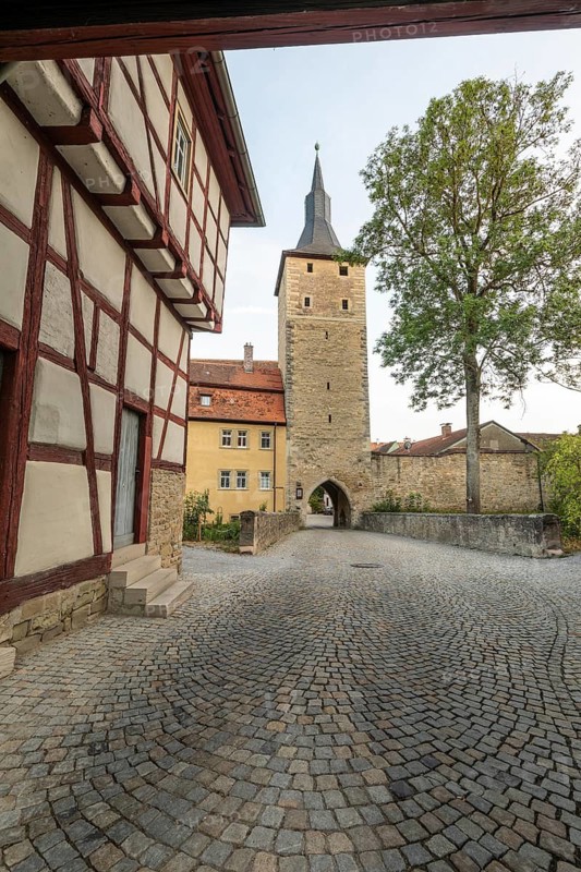 20 August 2026, View of the historic town gate and half-timbered house along a cobblestone street in Iphofen, Bavaria, Germany