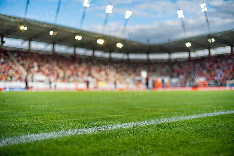 Professional soccer field with green grass and blurred stadium crowd under bright floodlights, creating a dynamic background for football and sports concepts in Lubin, Poland