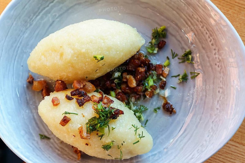National dish of Lithuania Cepelins, Cepelinai or zeppelins, potato dumplings made from grated and riced potatoes and stuffed with ground meat, dry curd cheese or mushrooms, Two dumplings served with crispy bacon and fresh herbs on a ceramic plate