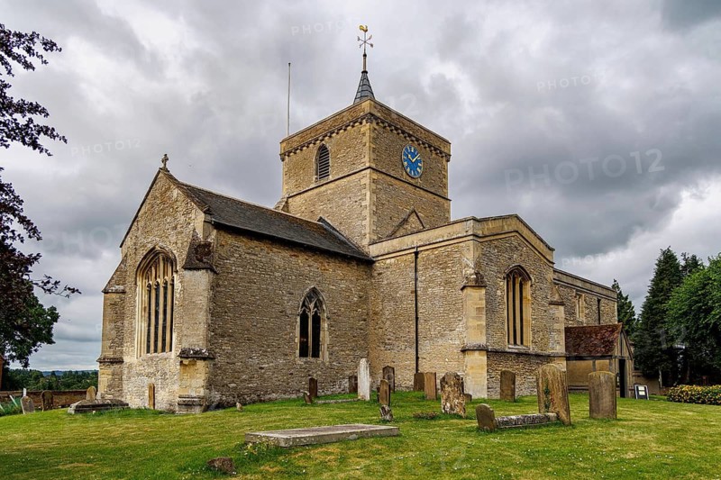 Full view of the medieval St James the Great parish church and its churchyard gravestones under a dramatic sky, Bierton, Buckinghamshire, United Kingdom