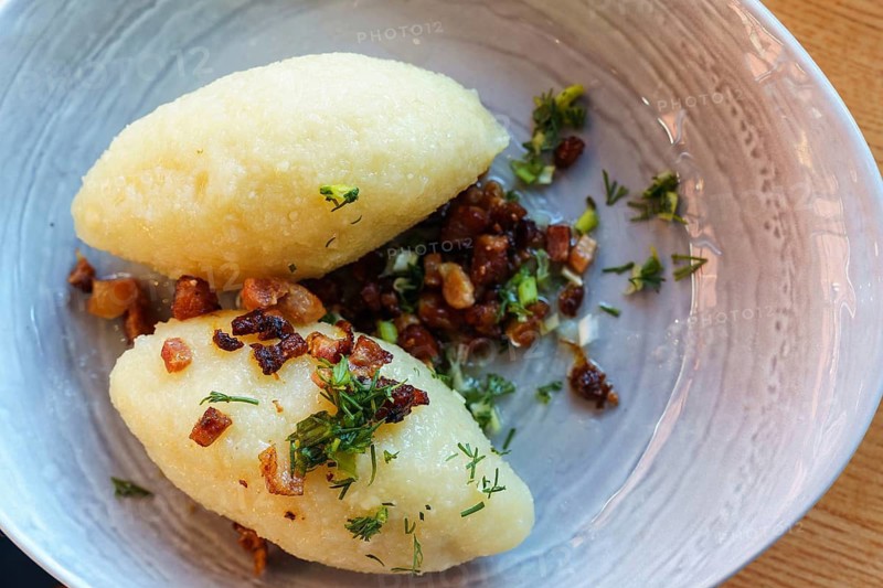 Lithuanian national dish zeppelins or Cepelinai or didzkukuliai with fried bacon and herbs, top view, Two potato dumplings garnished with onions and herbs in a bowl