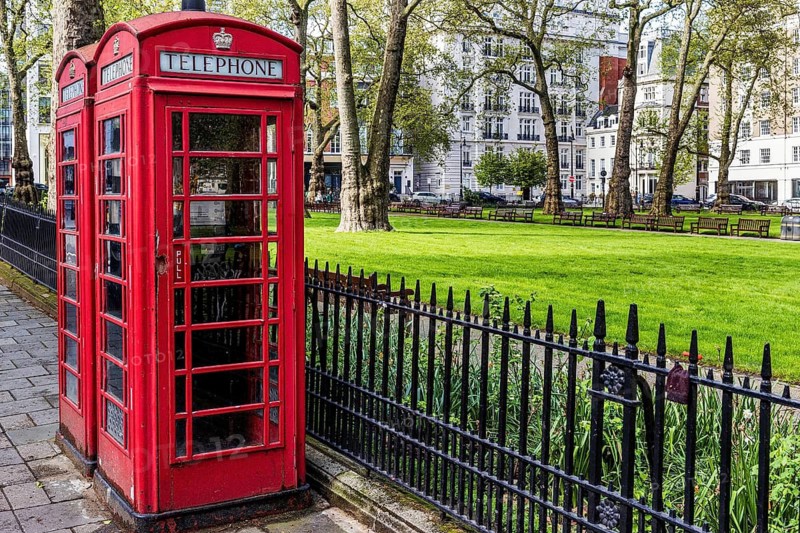Red telephone boxes stand beside the railings of Berkeley Square Gardens amid historic London Plane trees, Mayfair, England, United Kingdom