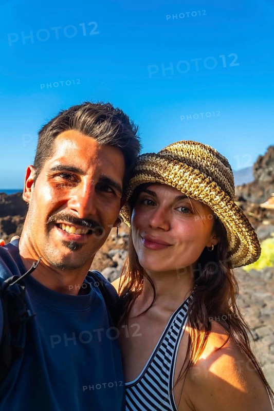 Happy couple taking a selfie together, smiling and enjoying their summer vacation at el hierro island in the canary islands, spain, with clear blue sky backdrop
