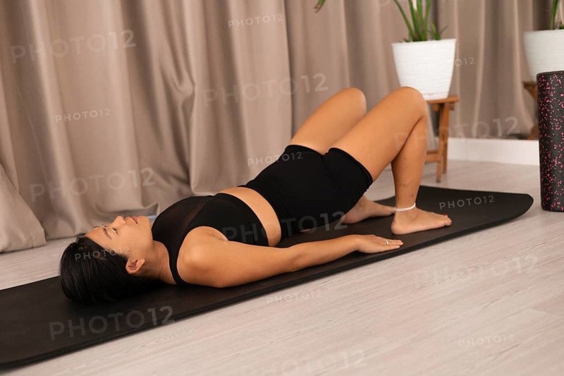 Woman relaxed on yoga mat, in a room with a plant and curtain
