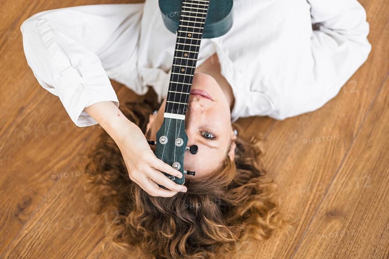Woman with a ukulele on a wooden floor, giving a serene and introspective vibe
