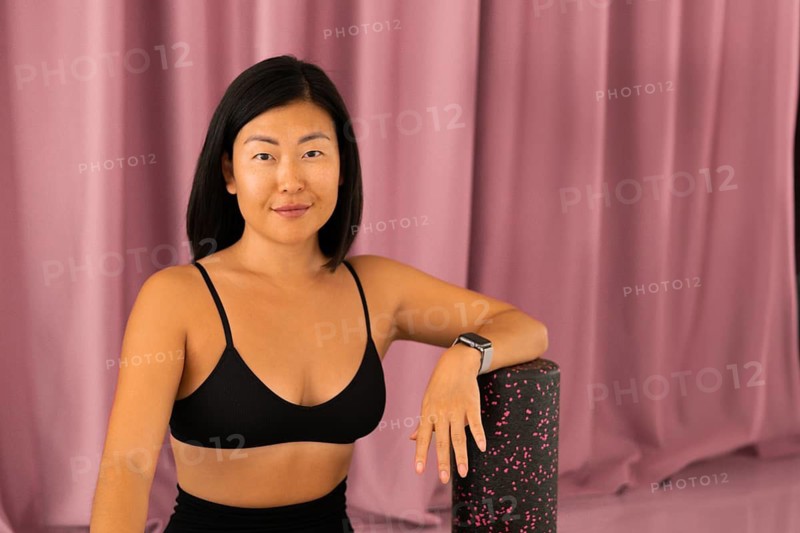 The woman leans on a foam roller, wearing a black top, exuding calm and confidence