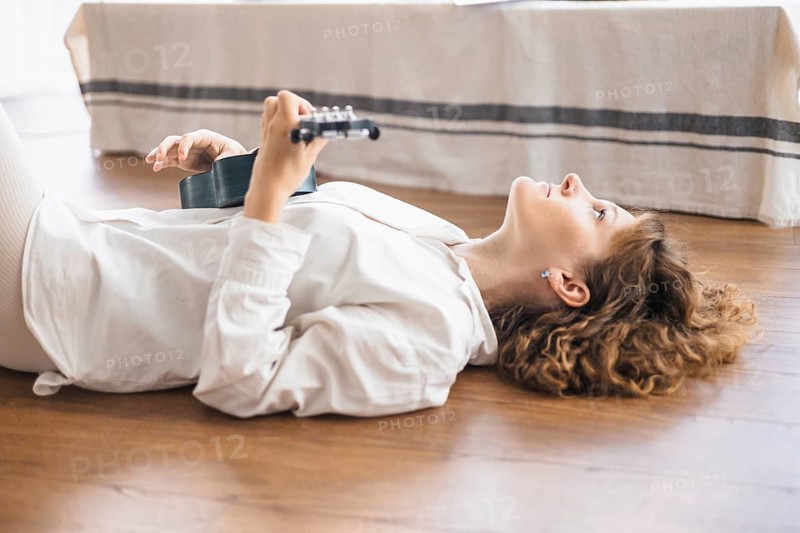 Person lies on a wooden floor with a ukulele, looking upward in a relaxed state