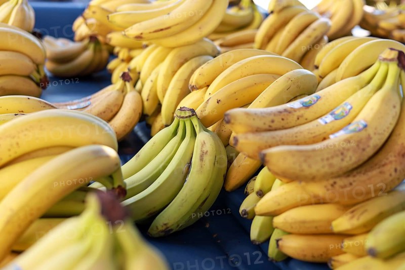 Stacks of ripe yellow bananas in bunches on display at a market, creating a vibrant tropical feeling