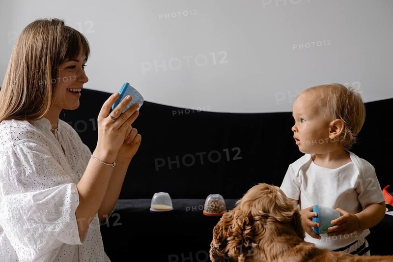 A mother and baby interact with colorful cups while a dog observes, highlighting playtime and companionship