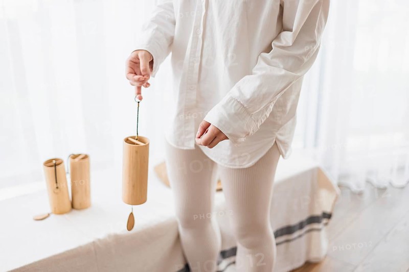 Person holding a bamboo wind chime in a bright room, dressed in white