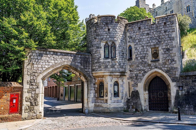 A small castellated gatehouse with a corner turret and pointed archways opens onto Chapter Mews, a historic cobbled area near St George's Chapel associated with the Dean and Canons and the domestic buildings of the collegiate community, Windsor, England, United Kingdom