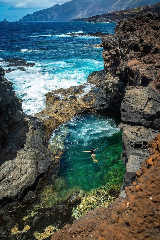 Woman enjoying a refreshing swim in a beautiful natural pool carved into volcanic rock formations along the rugged coastline of el hierro, immersing in clear turquoise ocean water during vacation