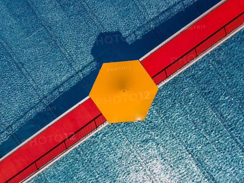 On a red bridge spanning a swimming pool at an open-air lido in Frankfurt, there is a yellow parasol in the centre. The deserted pool below is still waiting for the rush of bathers. The start of the swimming season is just around the corner. (Aerial view taken by drone), Eschersheim, Frankfurt am Main, Hesse, Germany