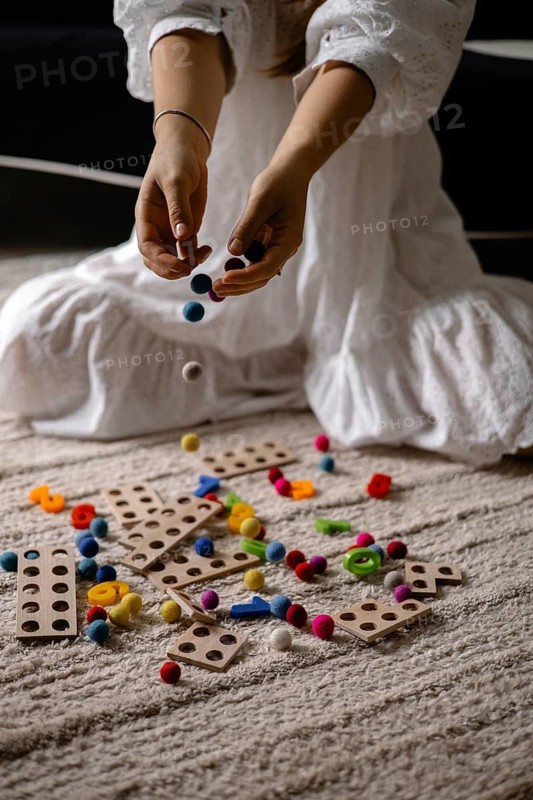 Person dropping colorful balls onto a mix of scattered wooden toys and balls