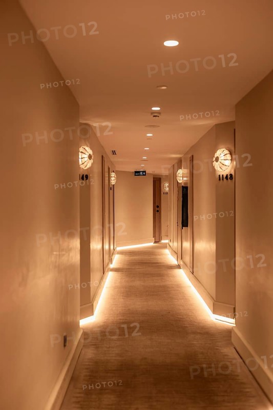 A well-lit hotel corridor with soft lighting and modern decor. The walls are painted in neutral tones, creating a calm atmosphere. Relaxing warm atmosphere