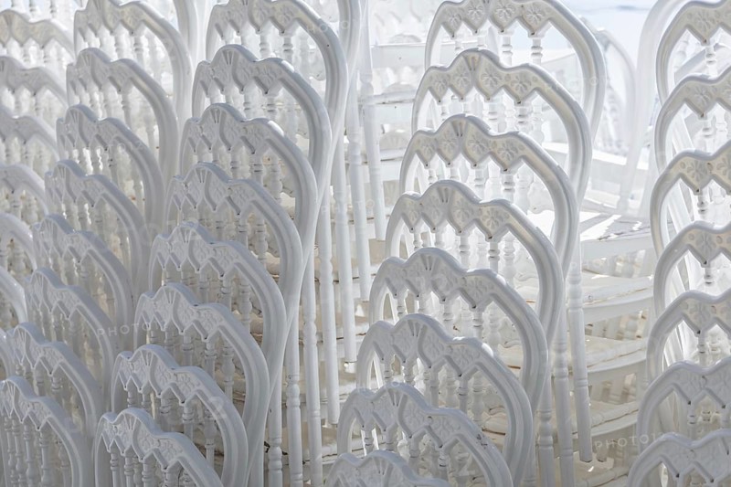 Stacked white plastic chairs create a uniform background texture. The chairs are arranged closely, showcasing their design and structure