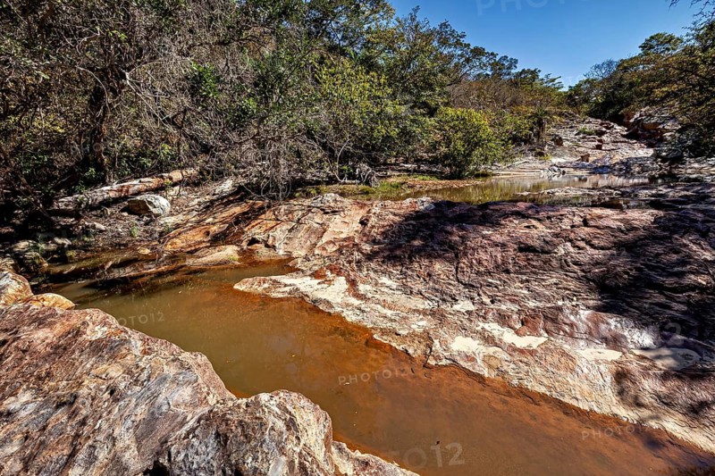 A dry riverbed with sparse water flow between rocky landscape and trees, a small river flows through the thorny savanna of the Caatinga of Bahia in Brazil