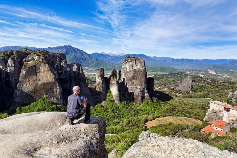 Hiker photographs views of hermitages between high rocks, monasteries on sandstone formations, Meteora, Cirrus, spring weather, Kalambaka, Thessaly, Greece